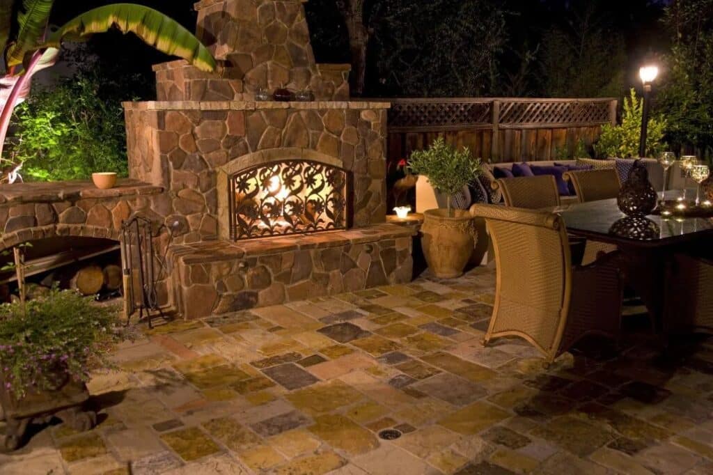 Elegant outdoor stone fireplace with intricate wrought iron detailing, surrounded by a custom paver patio and cozy seating area in Palo Alto, CA.