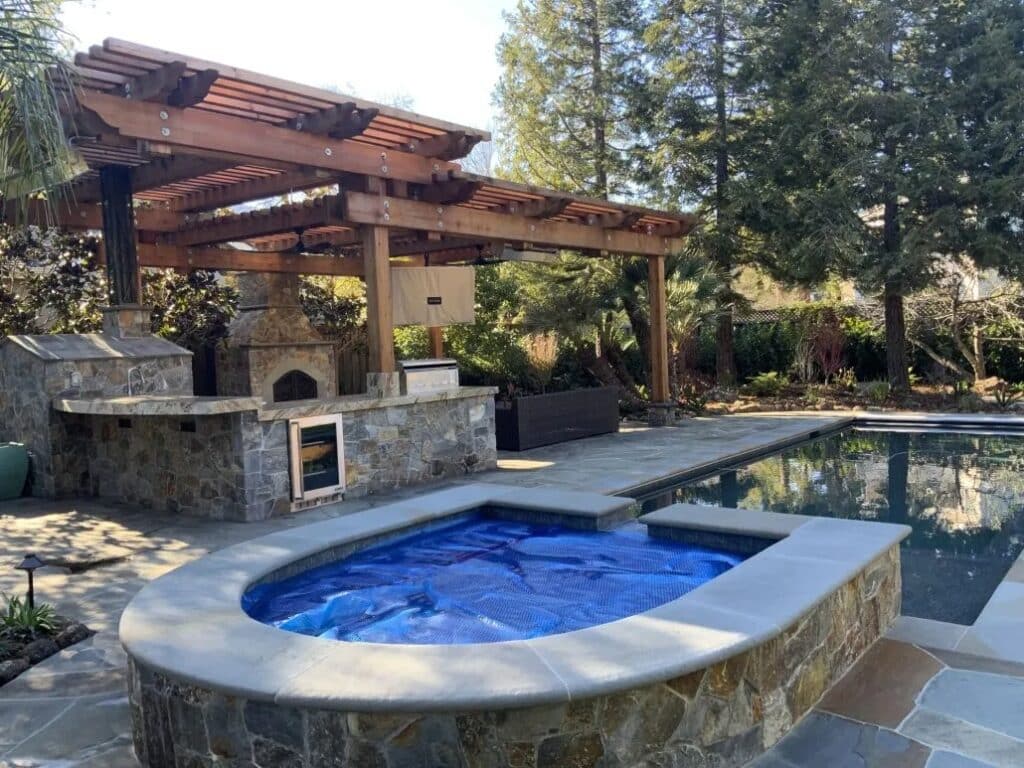 Luxury outdoor kitchen with stone bar, pergola, and poolside lounge in a Bay Area backyard.