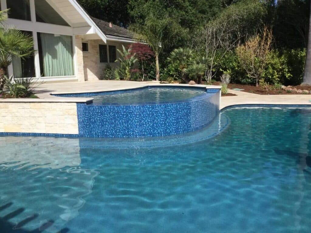 Infinity-edge swimming pool with elegant stonework and surrounding tropical landscaping in Saratoga.