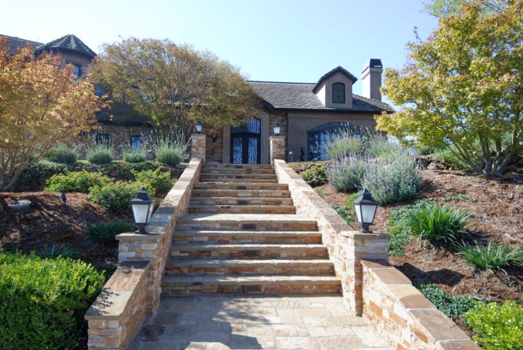 A dramatic stone staircase leading to a stately home, bordered by vibrant foliage and pathway lighting.