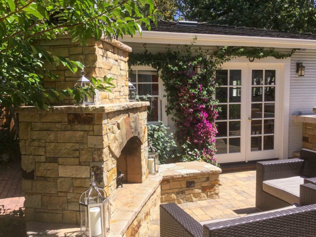 Custom stone outdoor fireplace with intricate masonry design, complemented by vibrant climbing bougainvillea and cozy patio seating, perfect for enhancing outdoor living spaces.